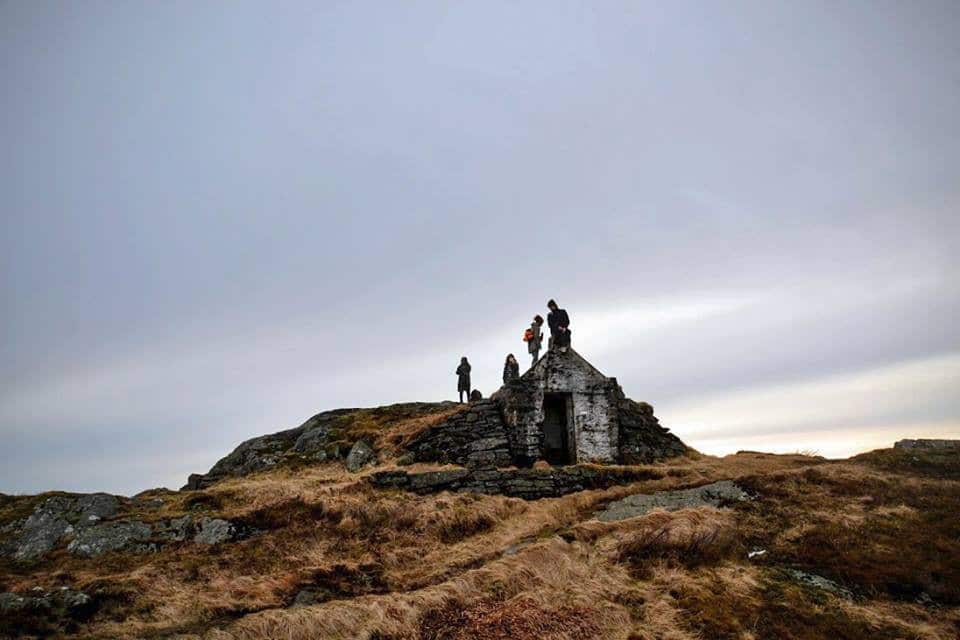 A group of people standing on the stone ruins that are Gallery Kronborg, located in a hilly and grassy landscape.