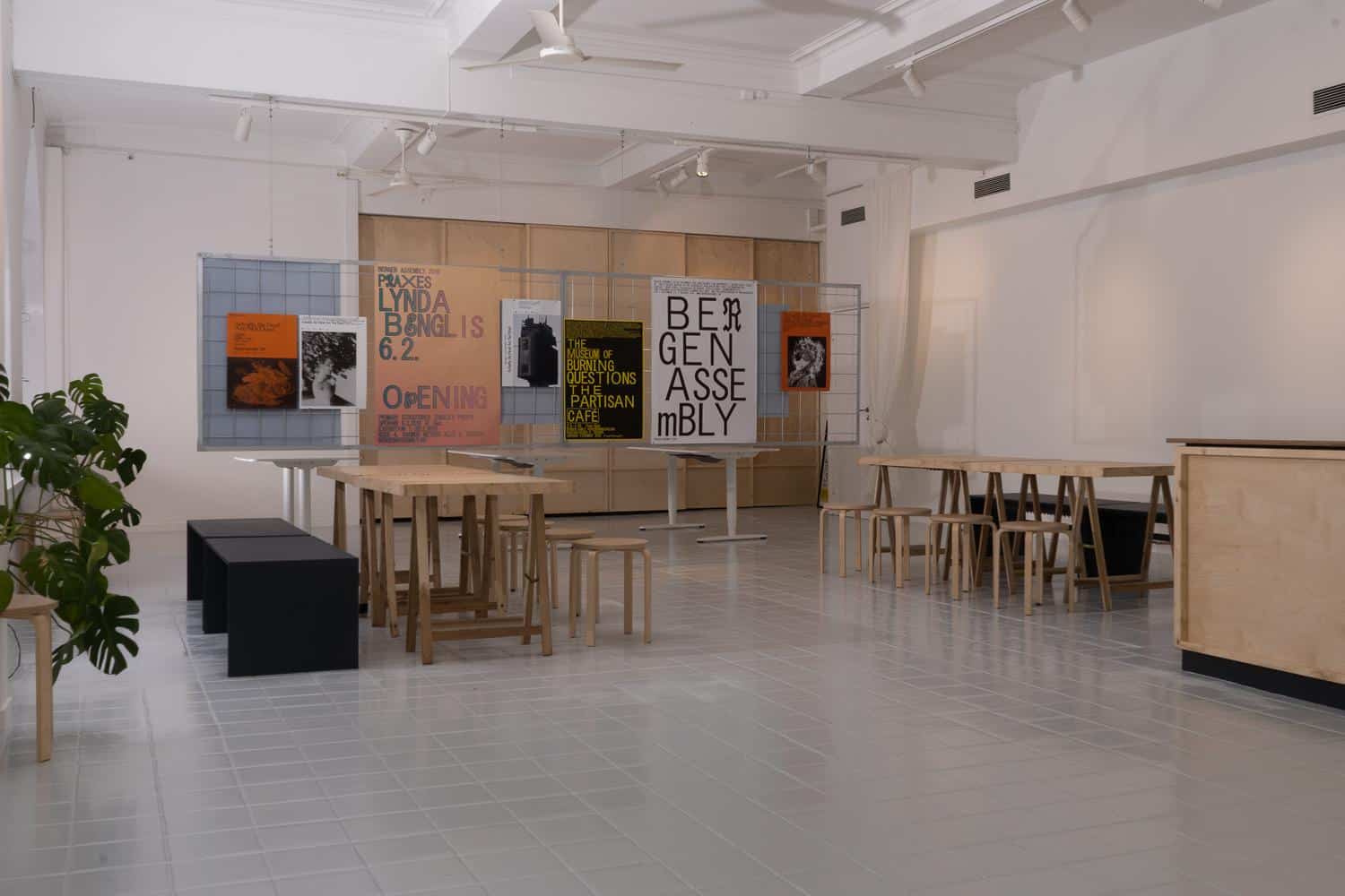 Modern art gallery interior of Bergen Assembly with wooden furniture, posters on display, and a potted plant. Neutral tones and minimalistic design create a spacious and inviting atmosphere.