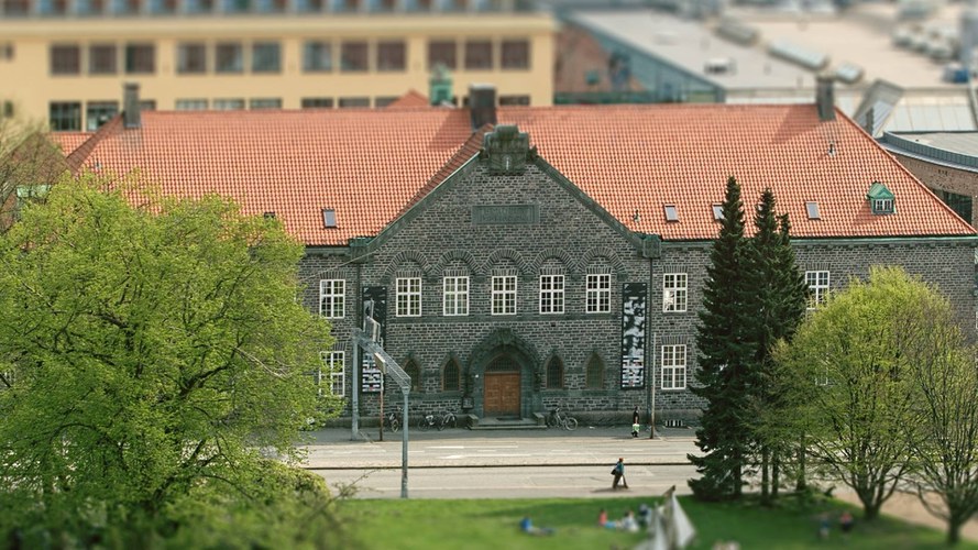 Bergen Public Library Main Library's building with a red-tiled roof, arched windows, and a central wooden door, surrounded by greenery and situated along a street with people walking nearby.